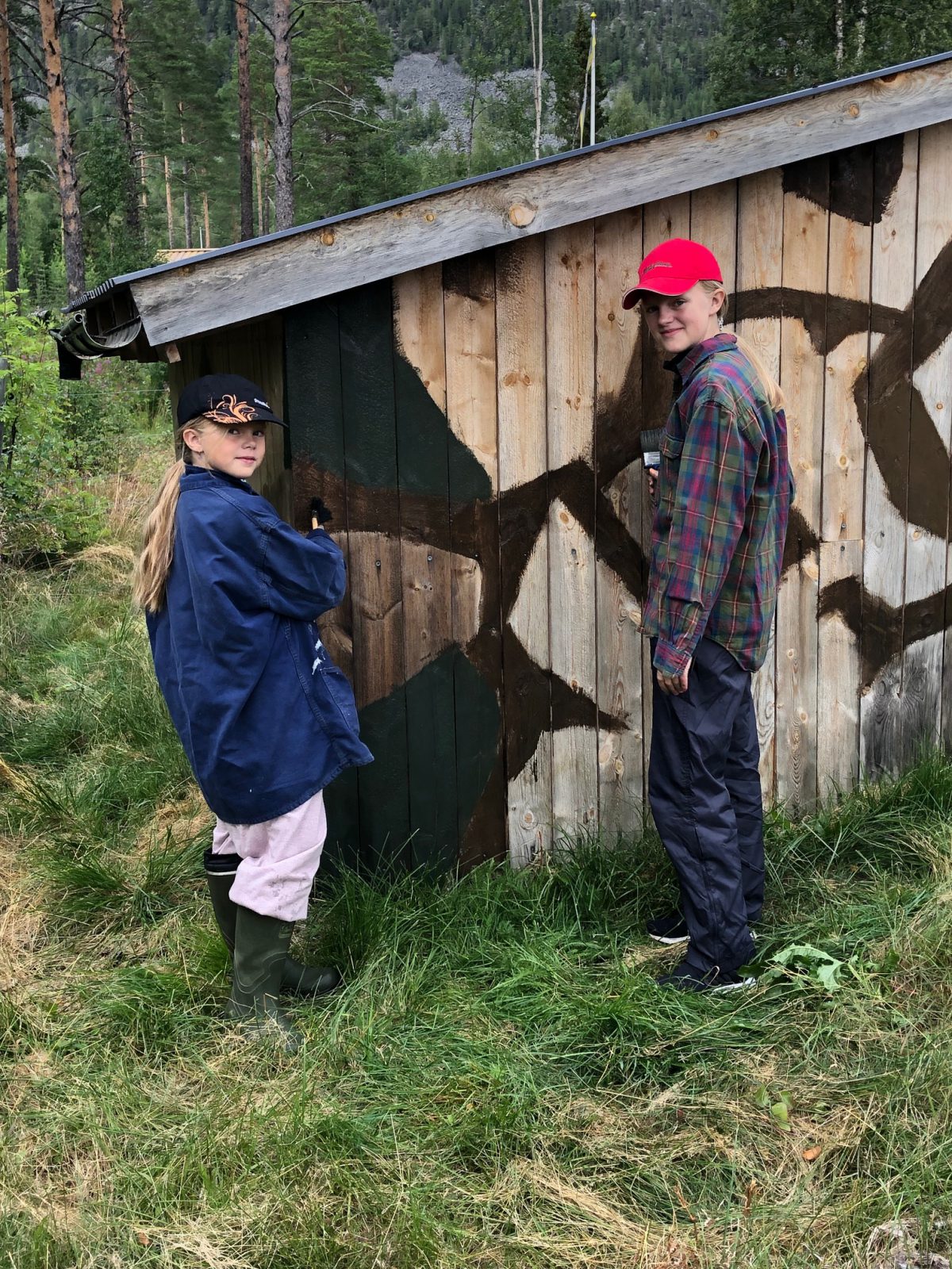 Elin och Emma Settling kamouflage-målar förrådsbyggnaden vid Långå Skans.